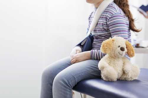 Kinderchirurgie Notfall Mädchen mit gebrochenem Arm sitzt auf Untersuchungsliege